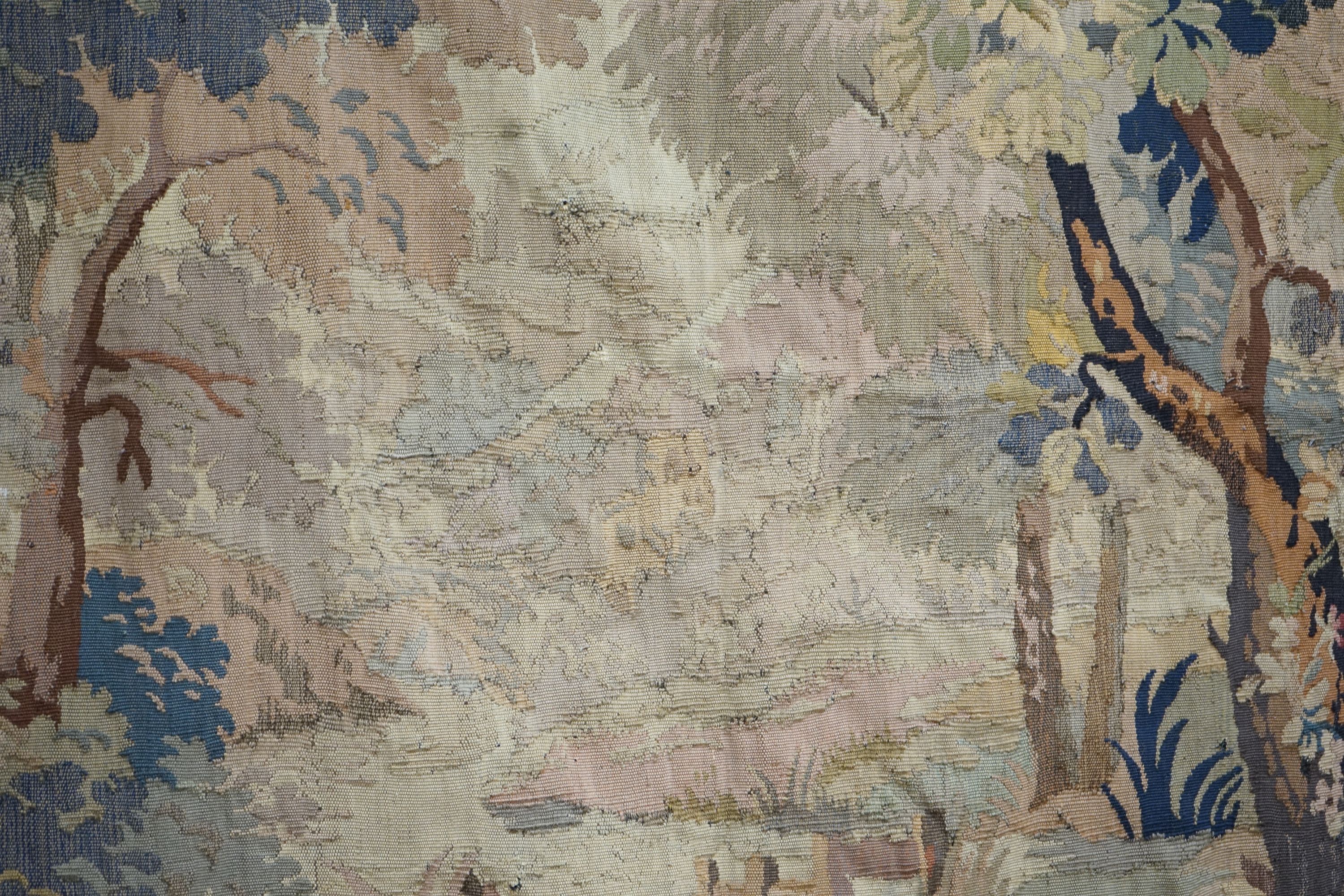 A late 19th / early 20th century French tapestry depicting a woodland scene with trees and flowers with a floral border woven in autumnal colours